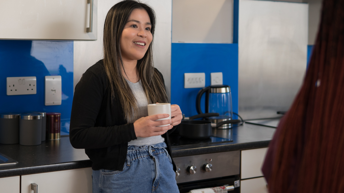 A student stood in a kitchen, holding a cup of tea and talking