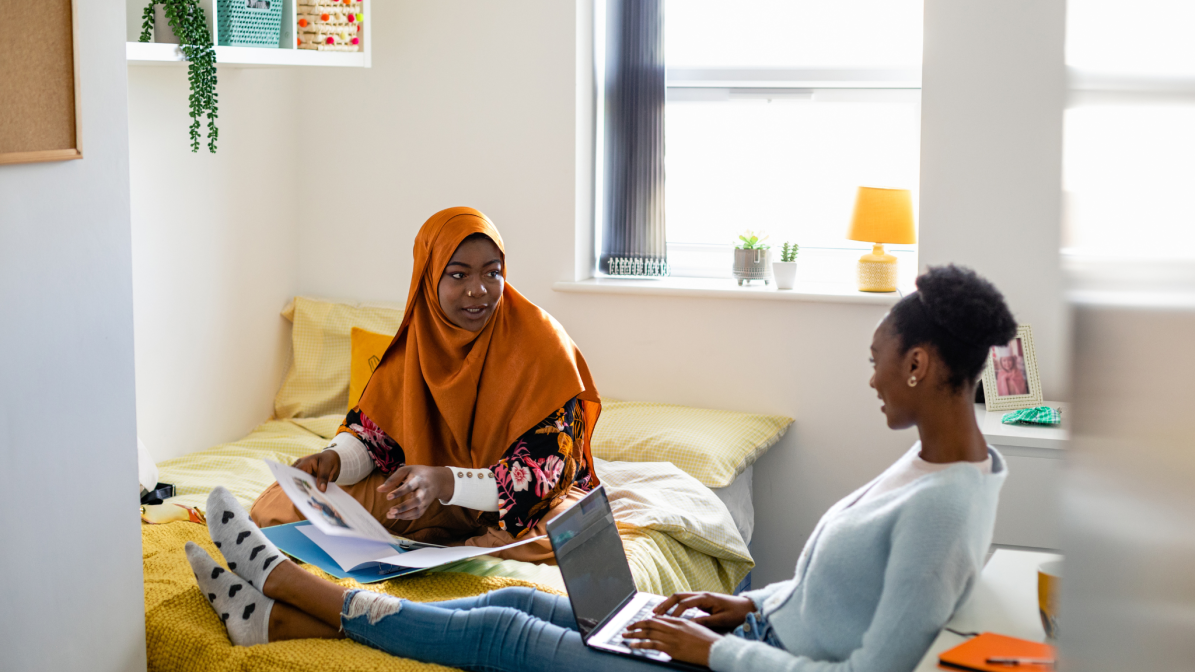 Two students sat on a bed talking