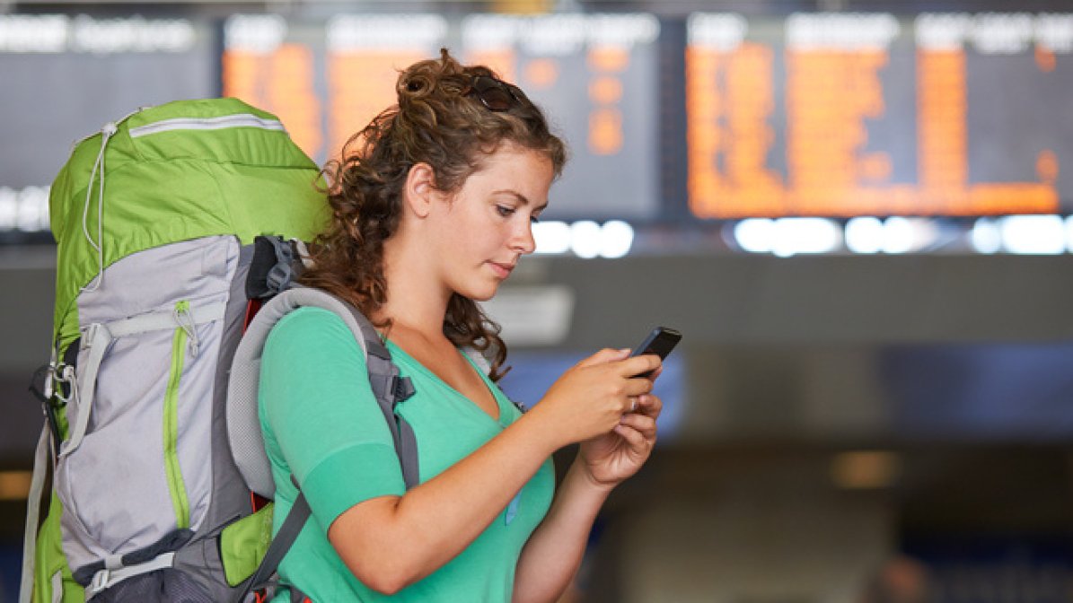 Gap year student at station looking on mobile phone 