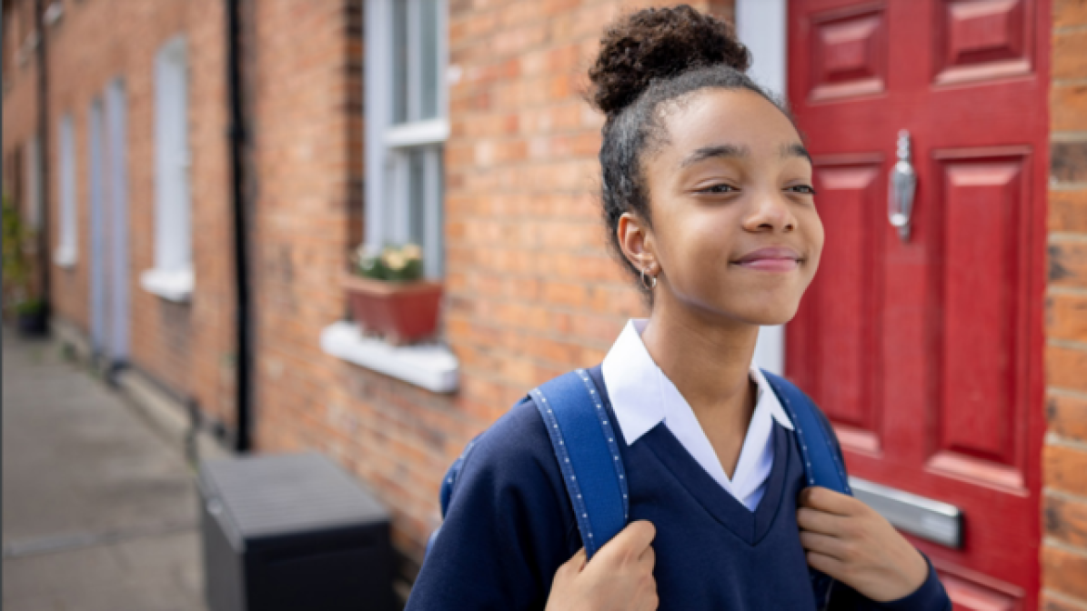 Schoolgirl walking down street carrying rucksack 