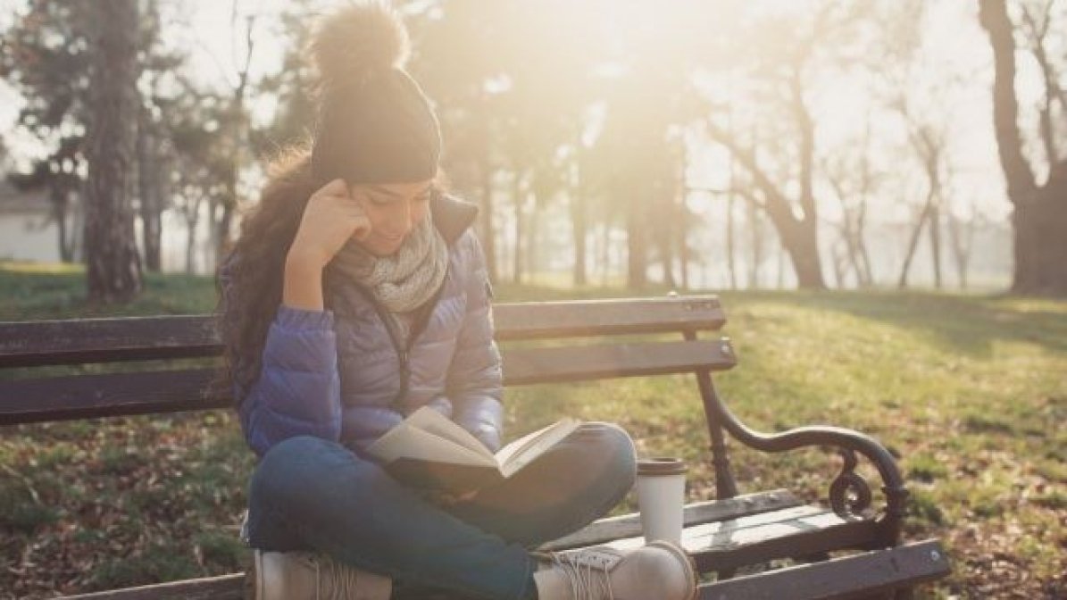 Student reading a book on park bench