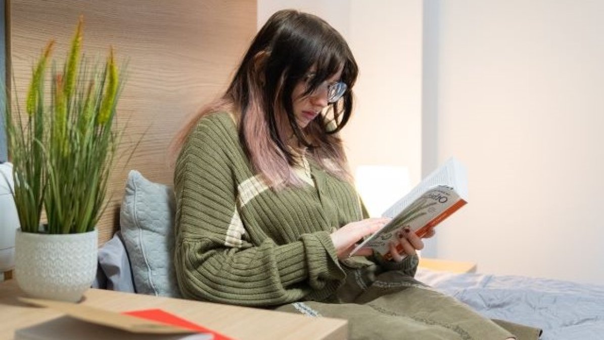 Student sitting on bed reading a book