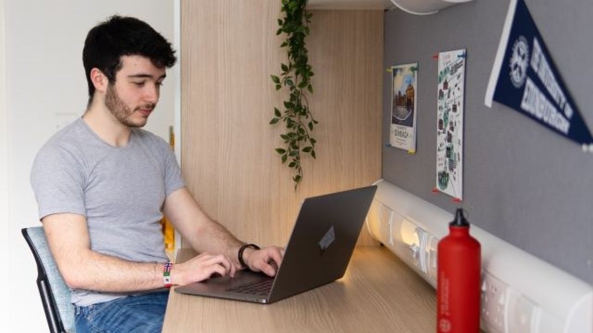 Student using laptop at desk in bedroom
