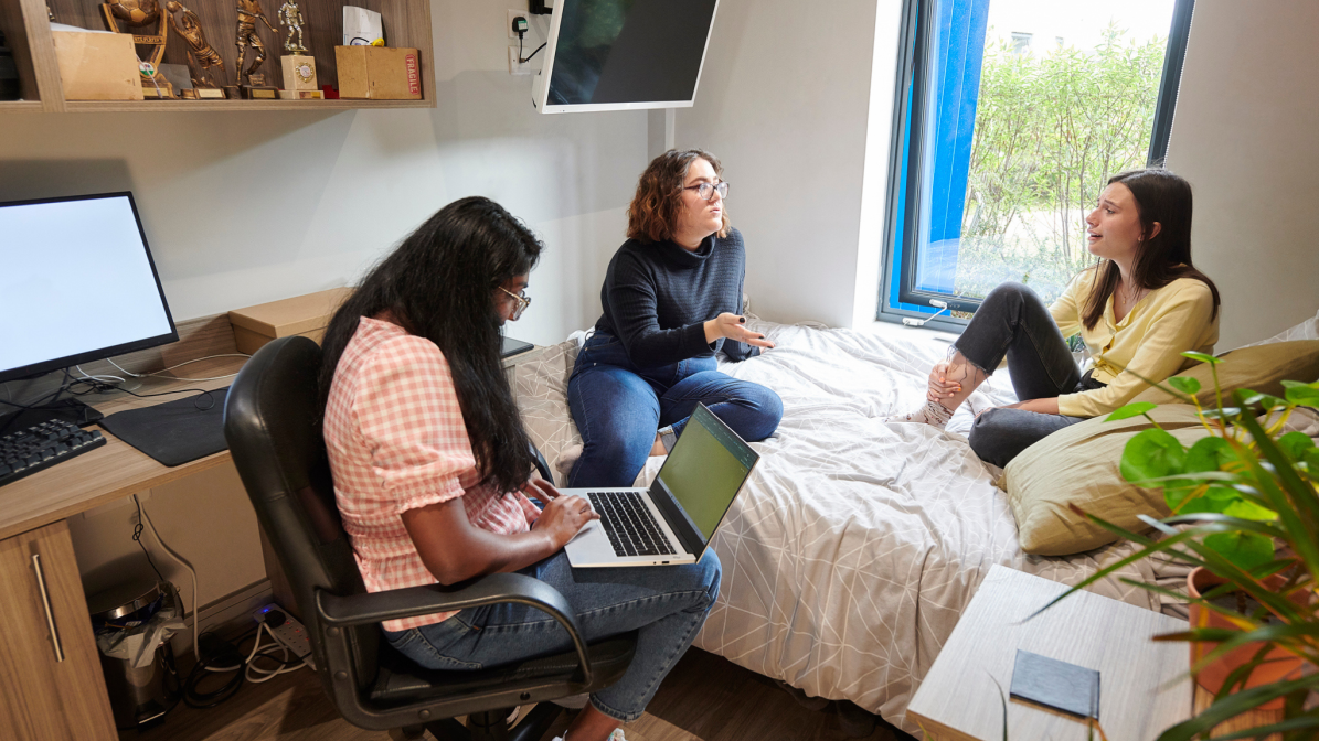 A group of three students sat talking in a bedroom.